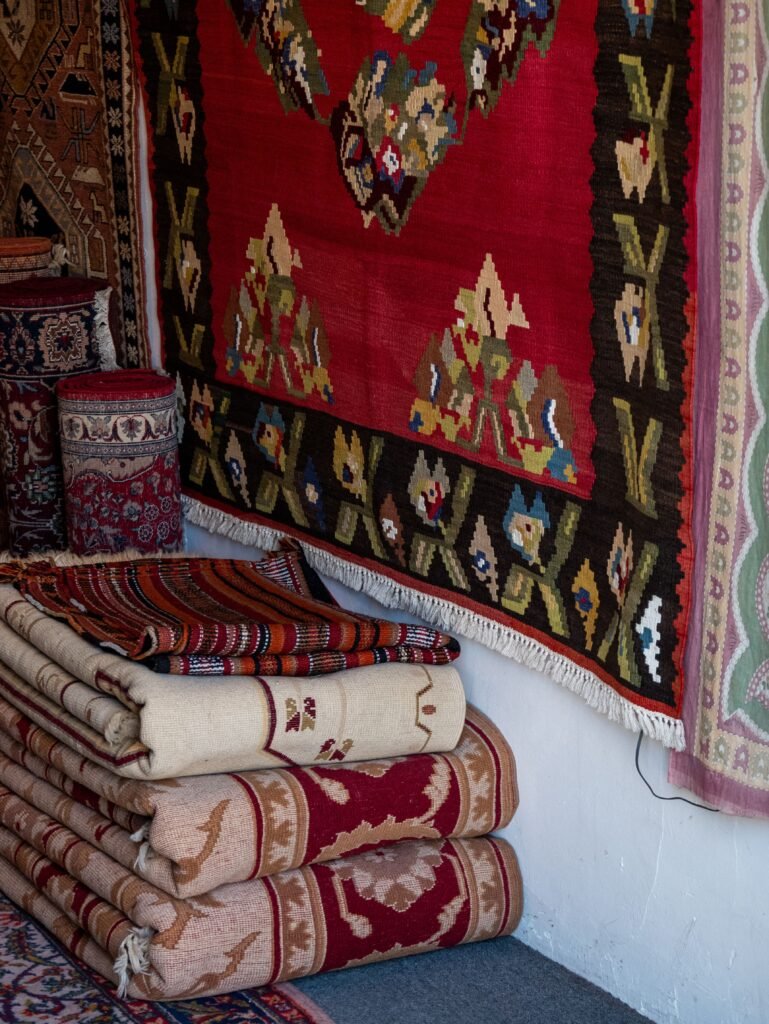 A vibrant display of traditional Oriental rugs with intricate patterns stacked and hung indoors.
